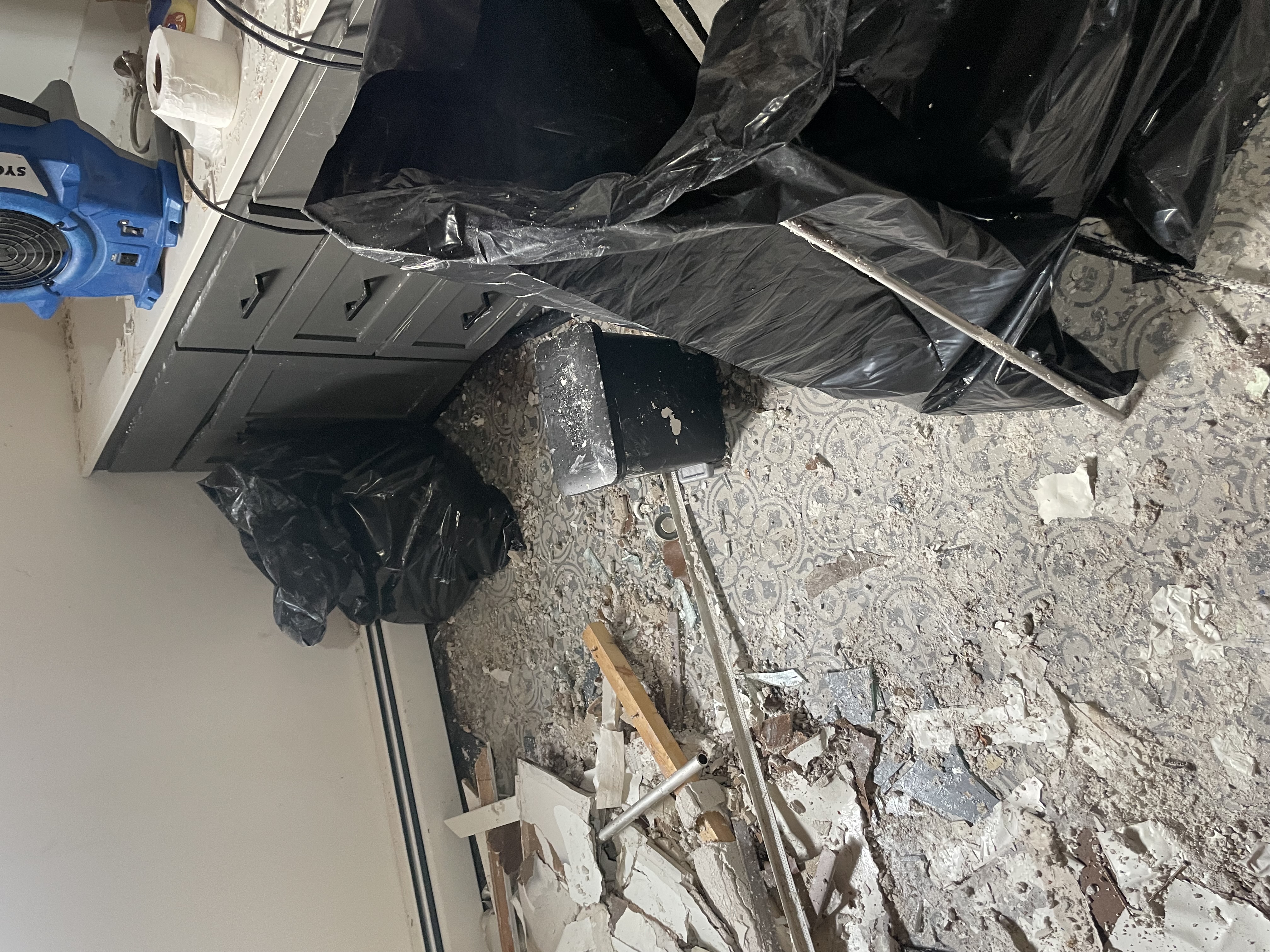 Severe water damage cleanup in progress showing professional restoration equipment including blue air mover, debris removal bags, and damaged materials being properly contained and removed from a residential property