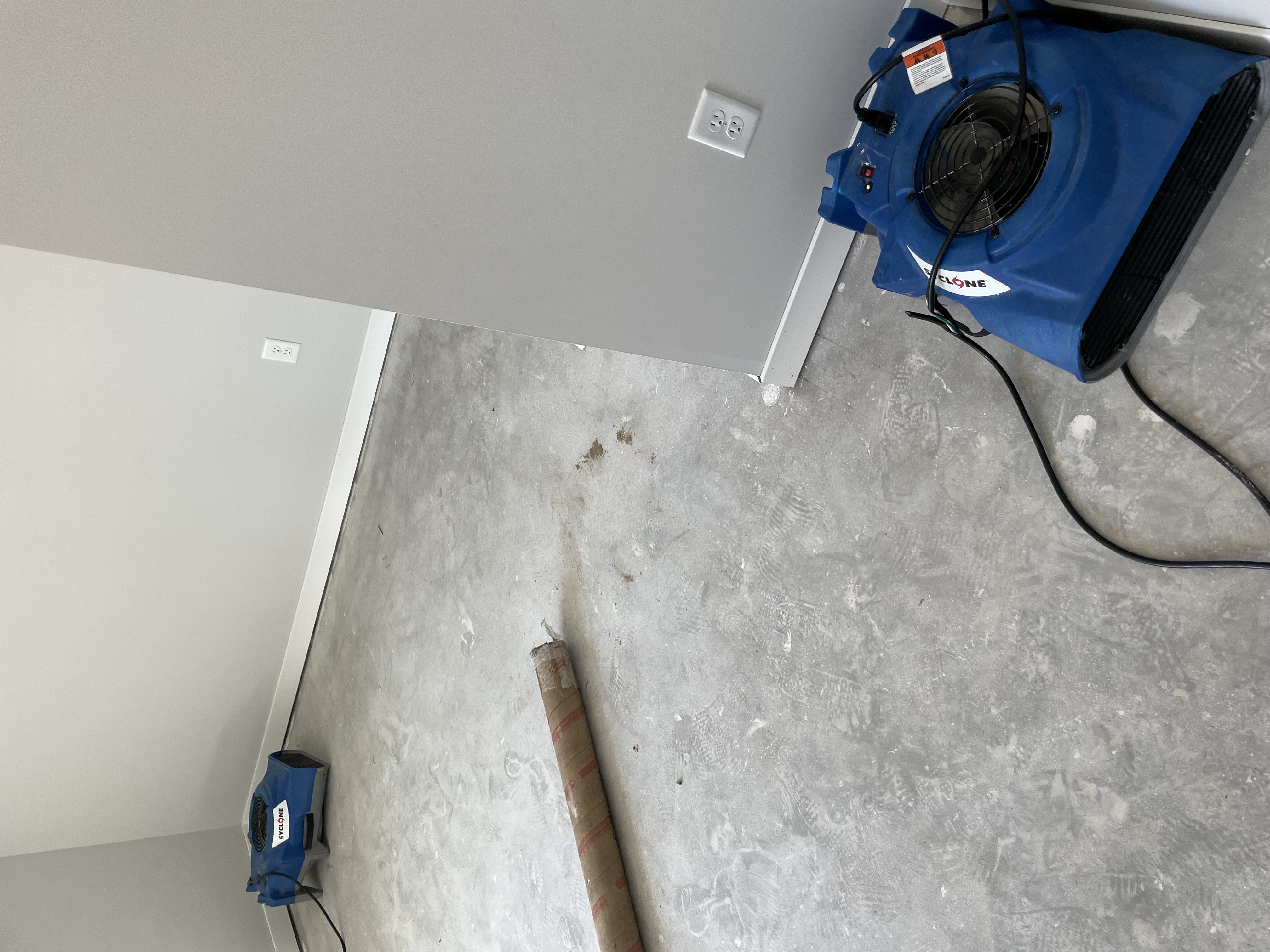 Multiple blue air movers positioned in room with concrete floors during active water damage restoration process Minneapolis Minnesota