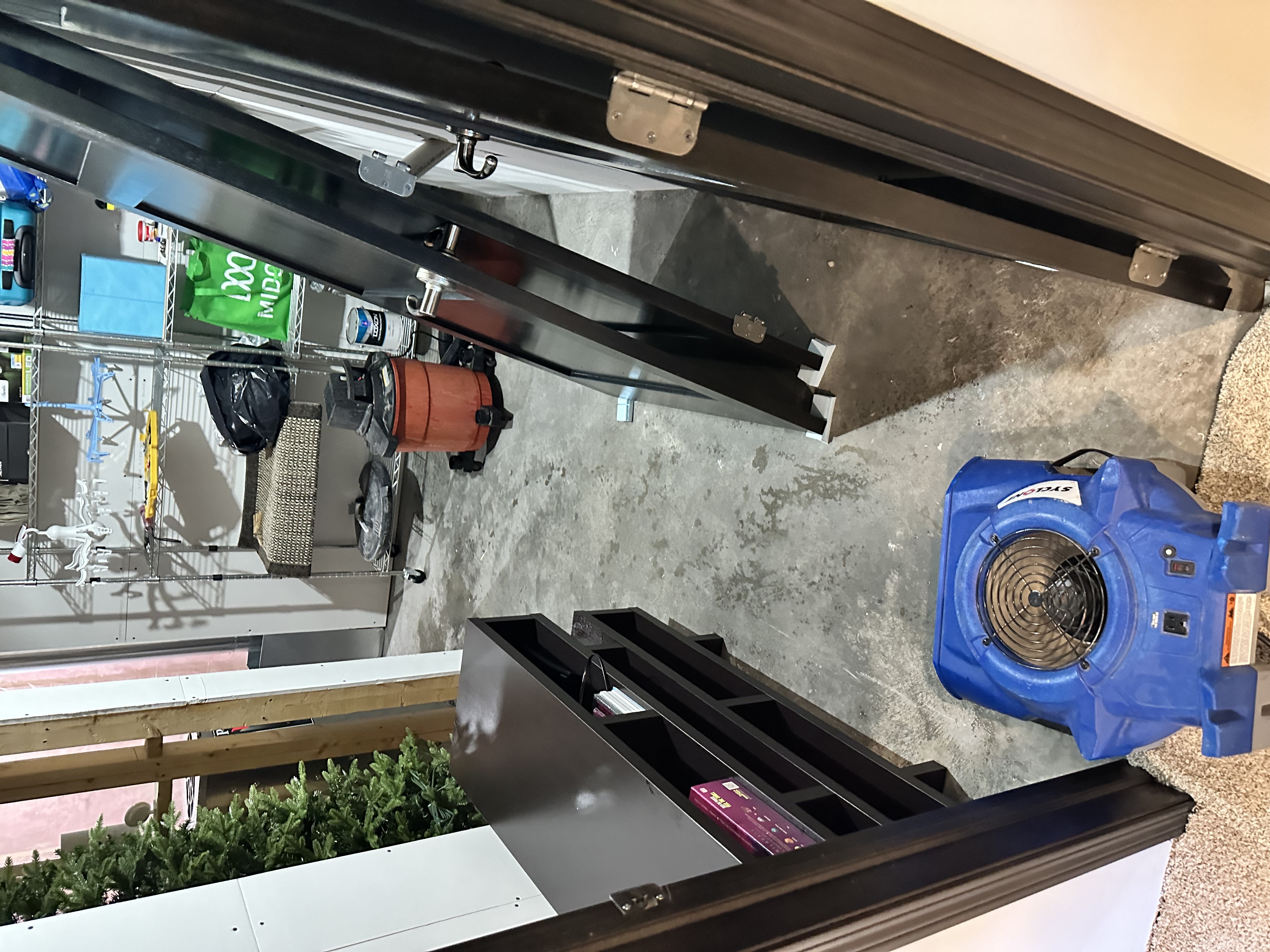 Professional restoration equipment setup in basement with blue air movers, metal shelving, and concrete floors during water damage restoration Minneapolis